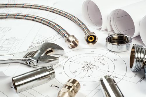 Assorted plumbing tools, fittings, and hoses laid out on top of detailed blueprints, illustrating a plumbing project plan.